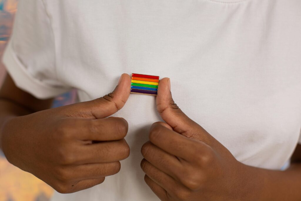 Black-skinned person holding tiny rainbow flag charm at the level of their heart
